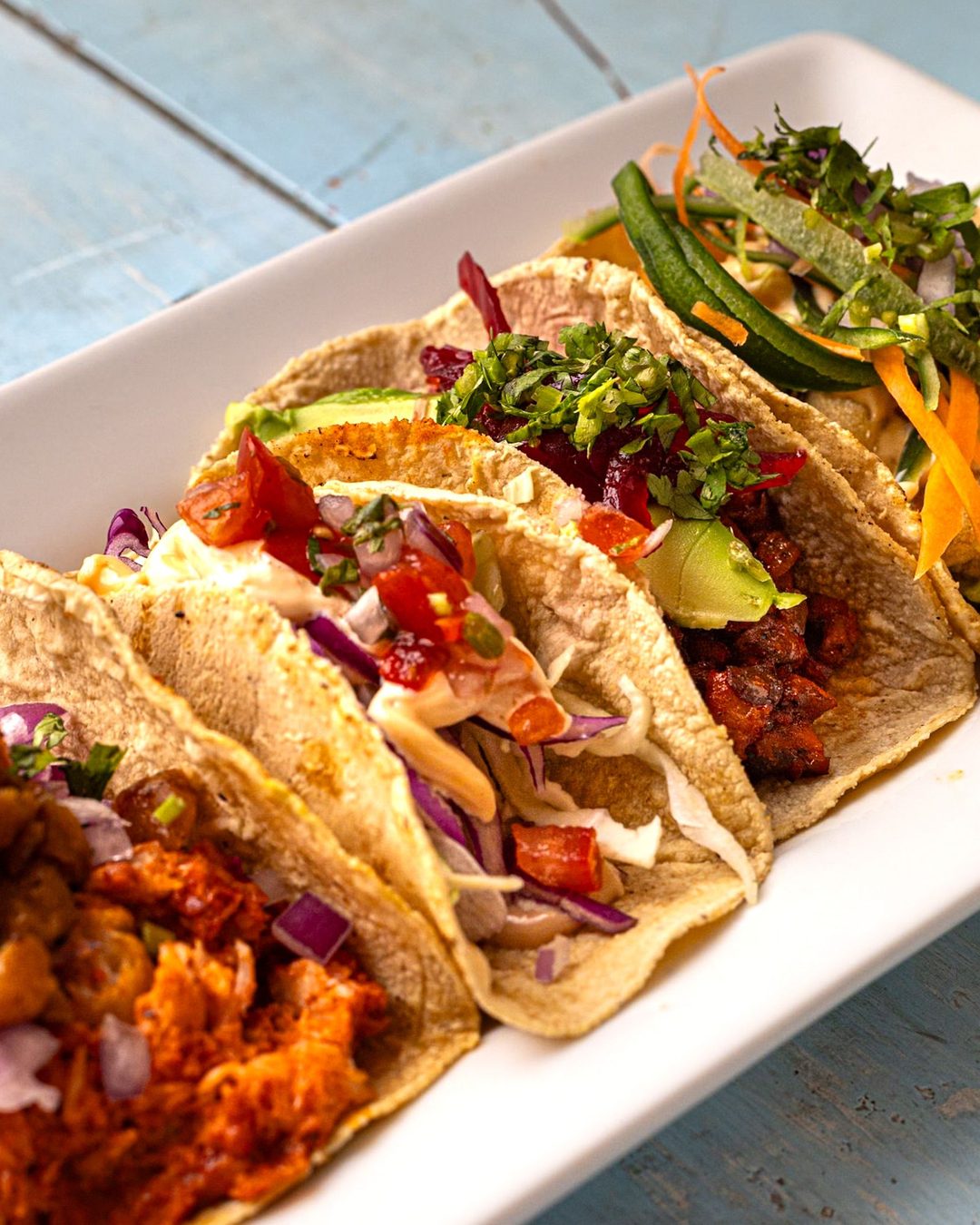 Four tacos with assorted fillings on a wooden table